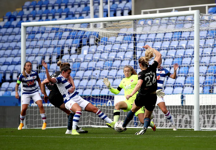 A woman football player shoots at goal surrounded by other players.