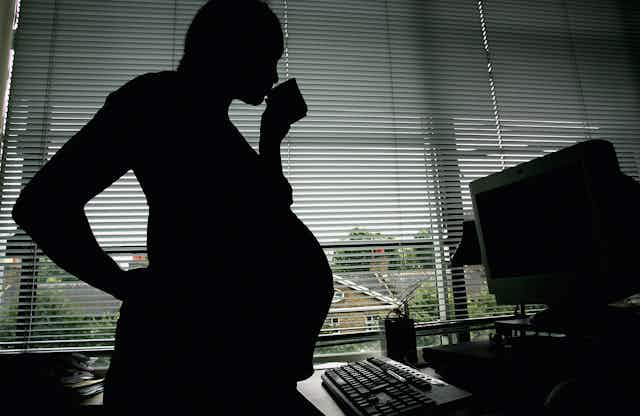 A pregnant woman stands in front of a computer.