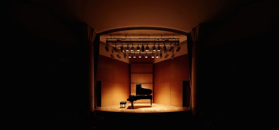 a spot lit piano in an empty, dark concert hall 
