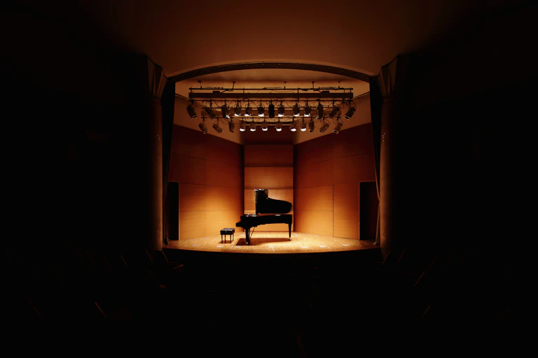 a spot lit piano in an empty, dark concert hall