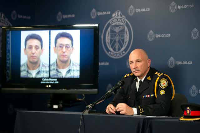 Police chief James Ramer sits in front of a TV screen displaying two mugshots of Calvin Hoover