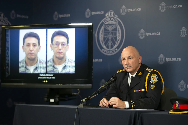 Police chief James Ramer sits in front of a TV screen displaying two mugshots of Calvin Hoover
