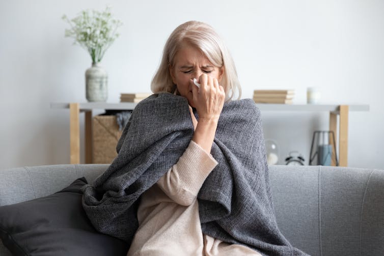 Sick woman sitting on couch with a blanket over her