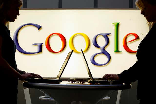 Google logo behind people working on computers.