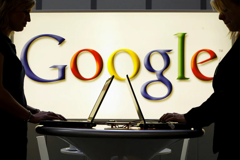 Google logo behind people working on computers.