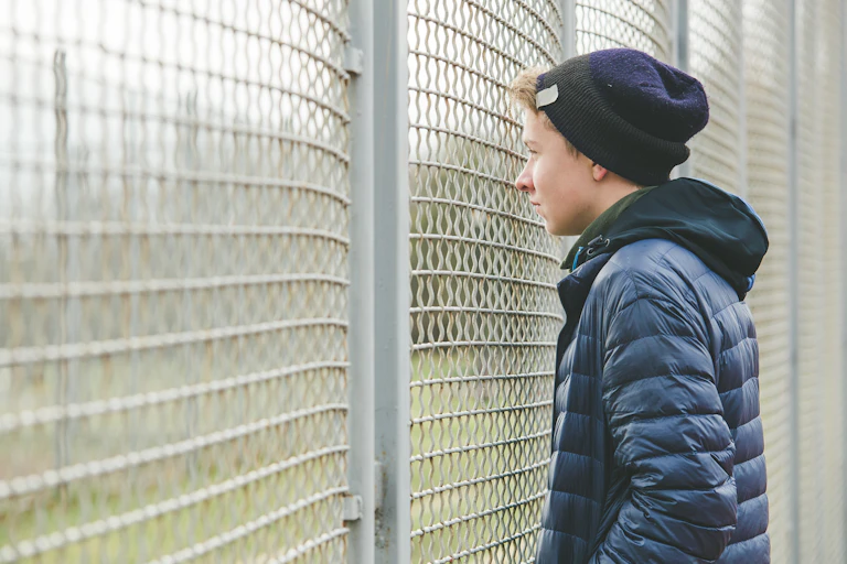 Teenage boys looking at sports field through the fence.
