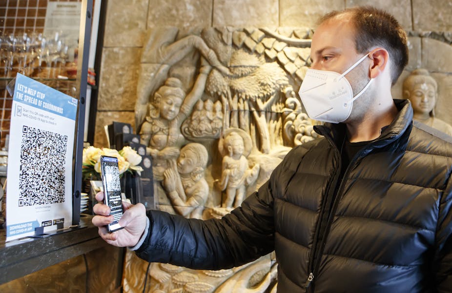 Man wearing face mask scans QR code with phone