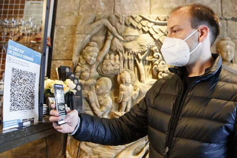 Man wearing face mask scans QR code with phone