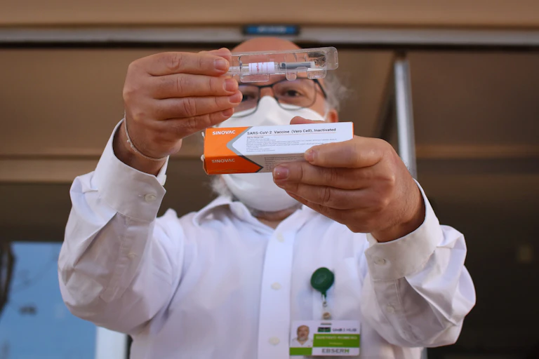 Man in a lab coat holds up a dose of Sinovac's coronavirus vaccine.