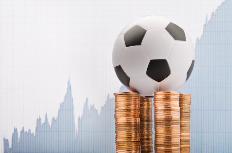 A football balanced on a pile of coins against a financial report backdrop.