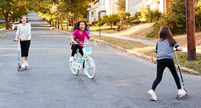 Three girls on bike and scooters in road