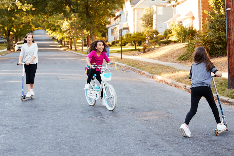 Three girls on bike and scooters in road