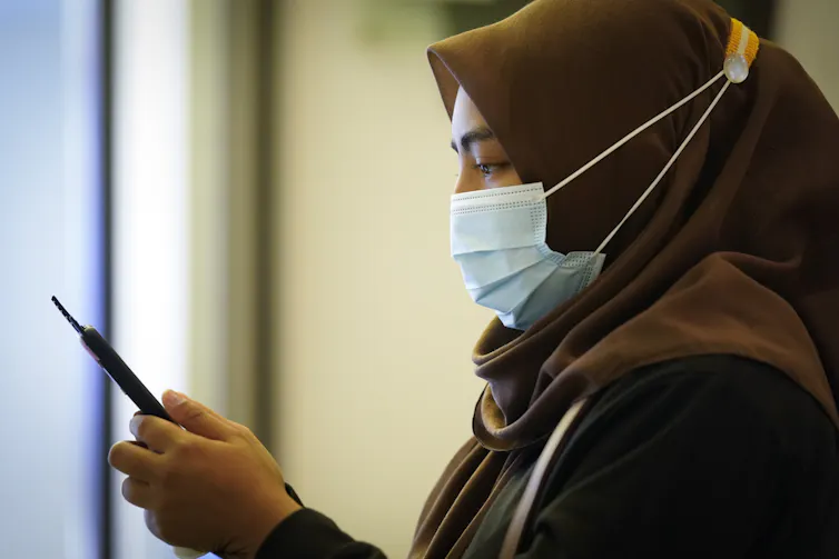 A woman wearing a mask looks at her phone