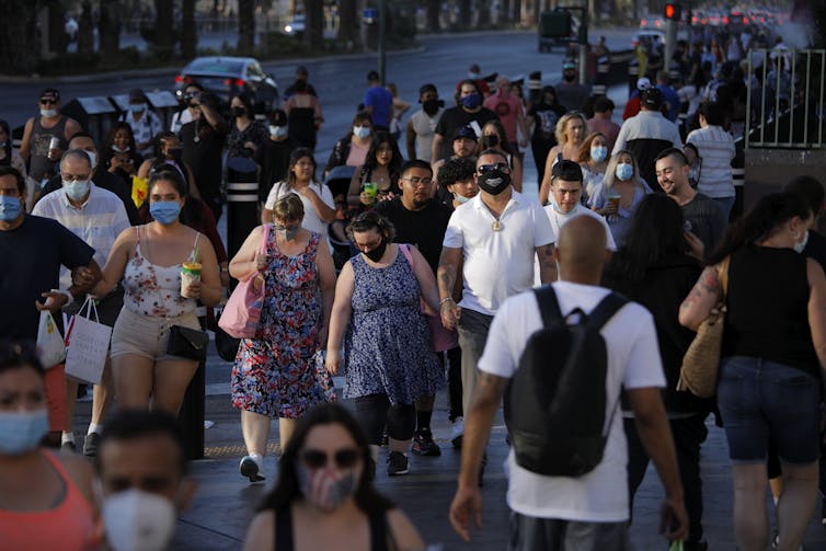 Crowds of people walking on sidewalks in Las Vegas, some wearing masks, some not.