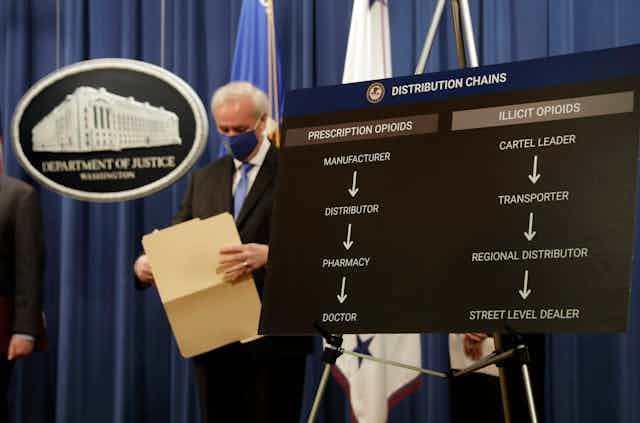 A man in a mask looks down while holding an open file folder at a Justice Department briefing.