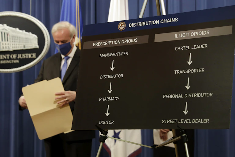 A man in a mask looks down while holding an open file folder at a Justice Department briefing.