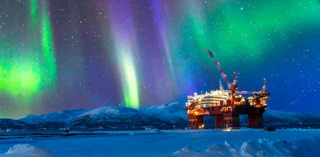 An oil platform in frozen landscape, sky lit by the Northern Lights.