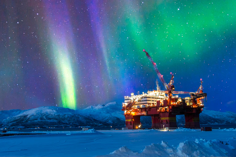 An oil platform in frozen landscape, sky lit by the Northern Lights.