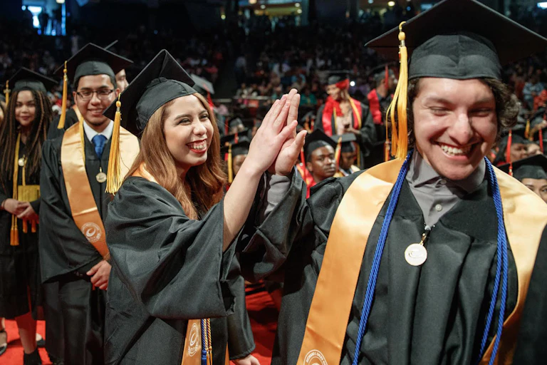 Nine young men and women in gradudation caps and gowns smile at a graduation ceremony.