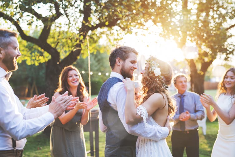 A couple dancing at their outdoor wedding, surrounded by guests clapping.
