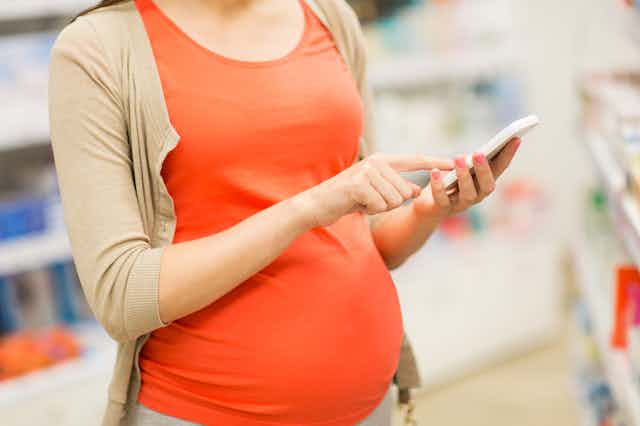 Pregnant woman using smartphone in shop or pharmacy
