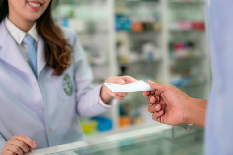 Person handing paper prescription to pharmacist