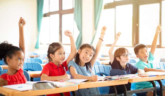 Elementary school children (including Vietnamese children)  raising their hand in class.