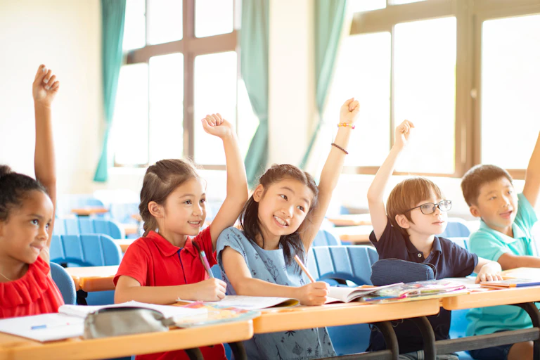 Elementary school children (including Vietnamese children) raising their hand in class.