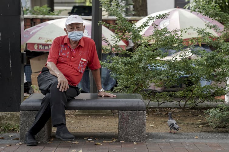 A man sitting on a bench in Singapore, wearing a face mask