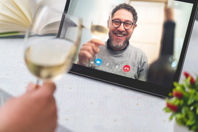 Man on video call screen holding glass of wine