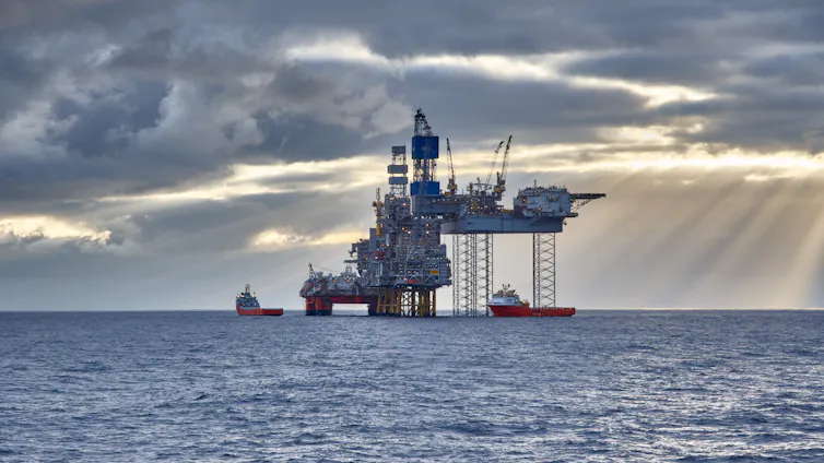 An oil rig in the North Sea with the sun streaming through the clouds over choppy water.