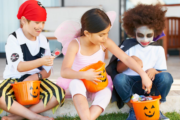 Three children dressed in Halloween costumes holding candy buckets while sitting down.