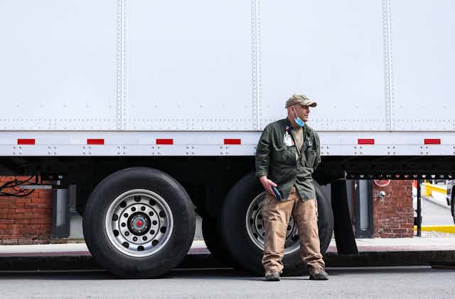 man with lowered mask leans against truck