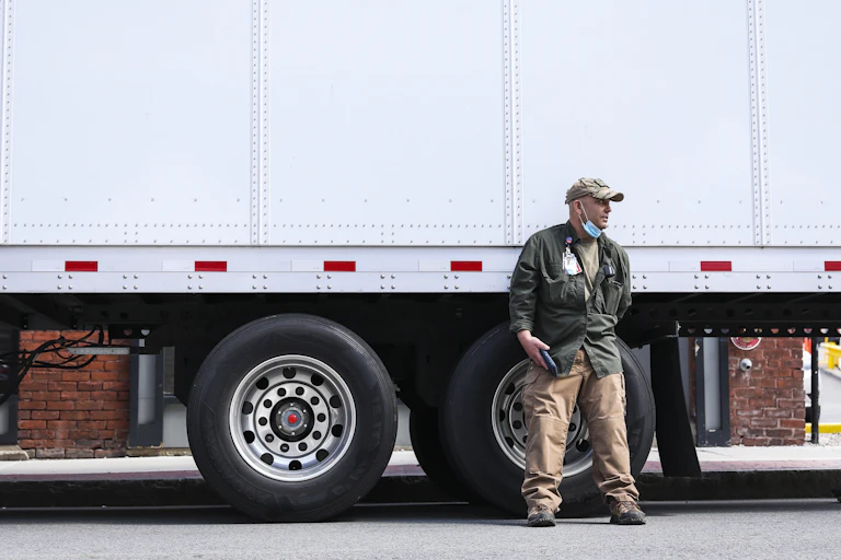 man with lowered mask leans against truck