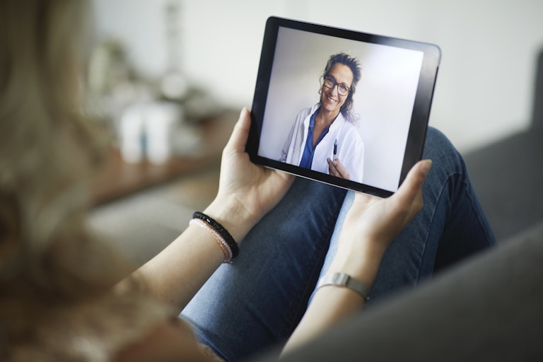 Young woman having online meeting with female healthcare person in white coat.