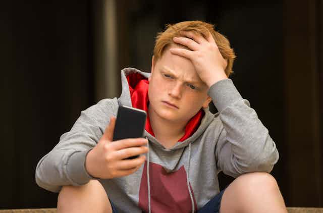 Boy looking at smartphone, clutching forehead, looking worried