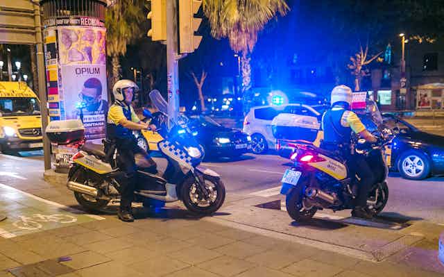 Policías locales de Barcelona en sendas motos, de noche, con las luces encendidas.