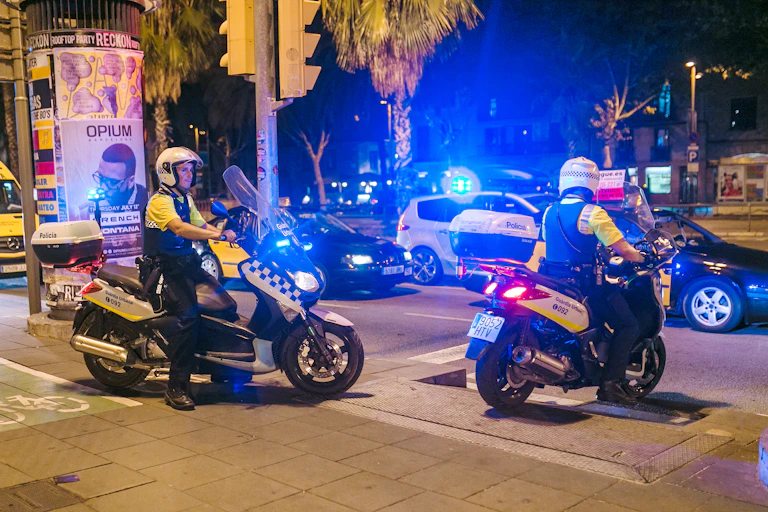 Policías locales de Barcelona en sendas motos, de noche, con las luces encendidas.