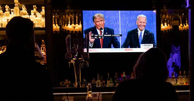People in a bar watching Trump and Biden on television.