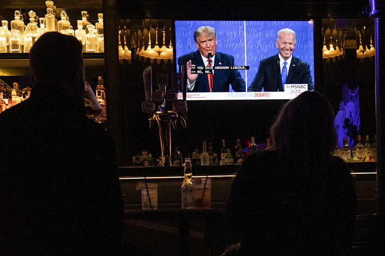 People in a bar watching Trump and Biden on television.