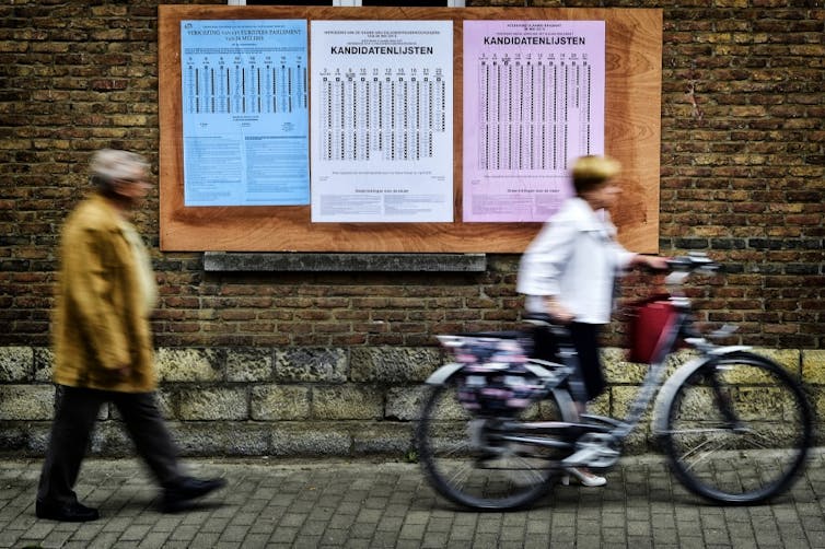 Des gens passent devant des listes de candidats