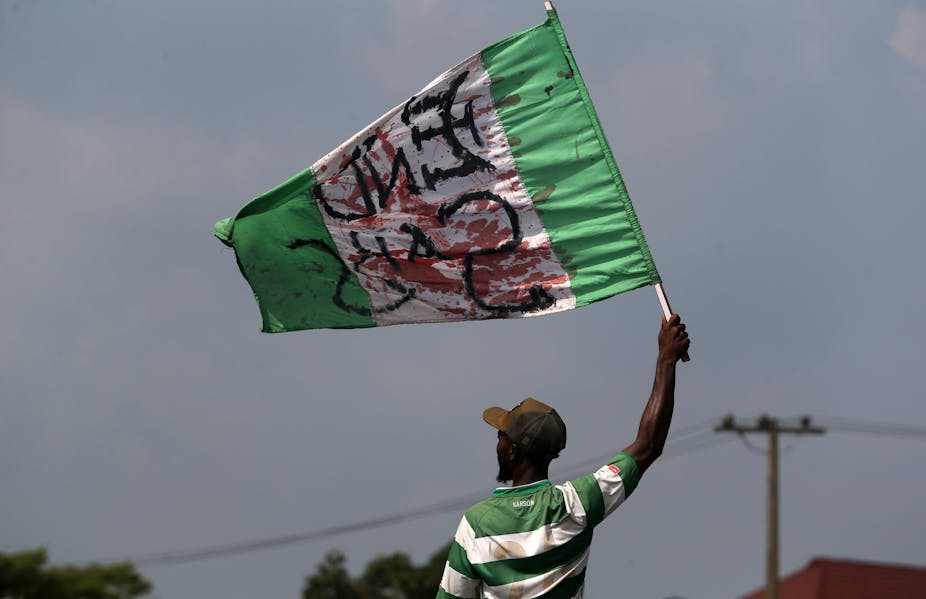 A man holds up a blood-stained Nigerian flag. 