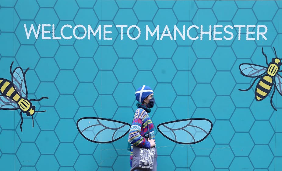 Woman with mask walking past Manchester sign