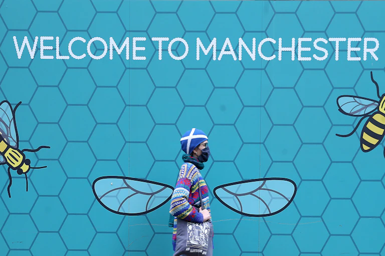 Woman with mask walking past Manchester sign