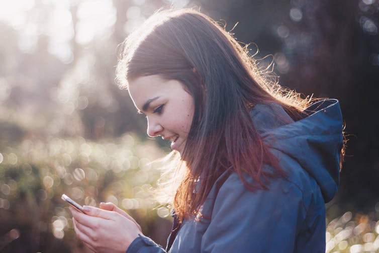 A teenaged girl looks at her phone outdoors.