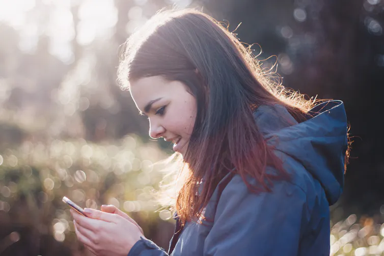 A teenaged girl looks at her phone outdoors.