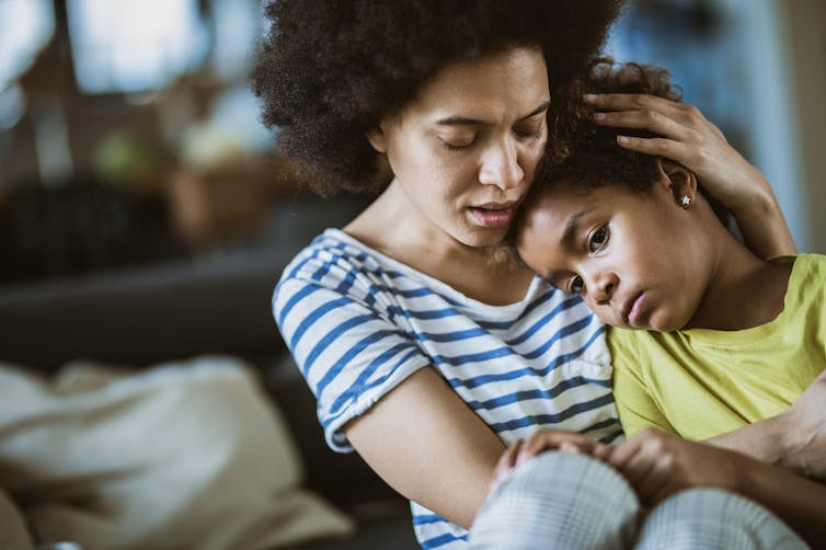 Young black mother comforting sad school age daughter at home.