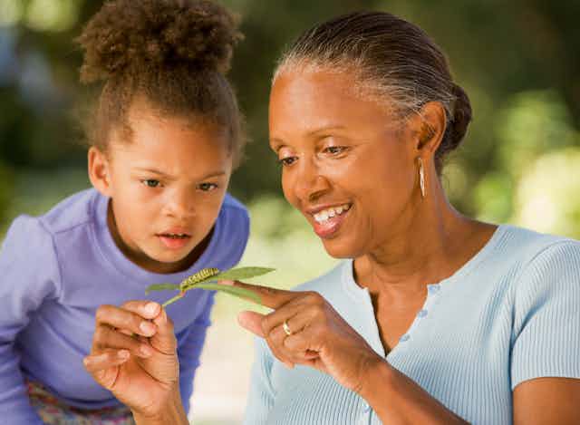 A young girl and a woman look at a caterpillar on a leaf. 