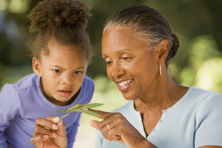 A young girl and a woman look at a caterpillar on a leaf.