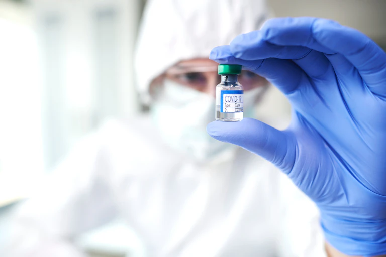 Investigador con guantes azules escrutando con la mirada una ampolla de medicamento covid